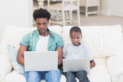 Father and son using laptops on the couch