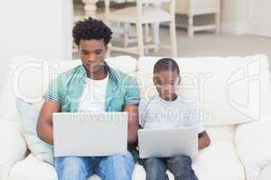 Father and son using laptops on the couch