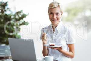 Young woman having a piece of pie using laptop