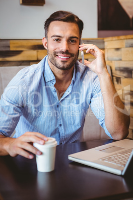 Smiling businessman on the phone with laptop beside