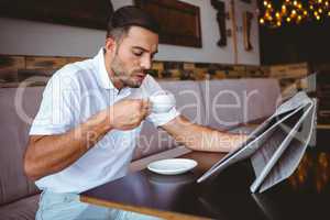Young man drinking cup of coffee reading newspaper