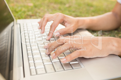 Pretty brunette lying in the grass and using laptop