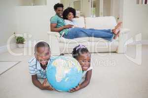 Happy siblings lying on the floor holding globe