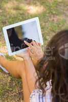 Pretty brunette sitting in the grass and using tablet