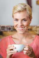 Pretty blonde woman smiling at camera and holding a cup of coffe