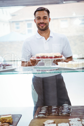 Smiling worker holding cupcakes behind the counter