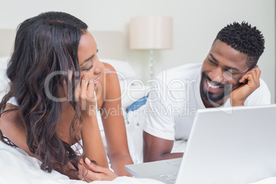 Relaxed couple using laptop on bed