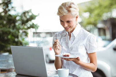 Young woman having a piece of pie using laptop