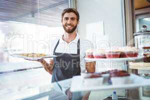 Smiling worker holding pastry behind the counter