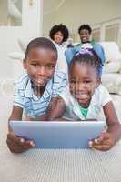 Happy siblings lying on the floor using tablet