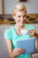 Pretty blonde holding cup of coffee and using tablet computer