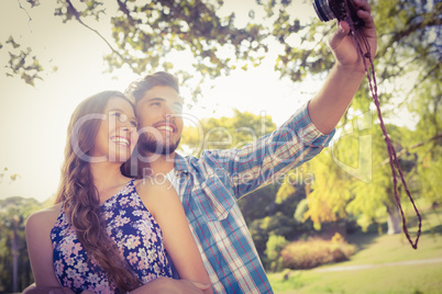 Cute couple doing selfie with retro camera in the park