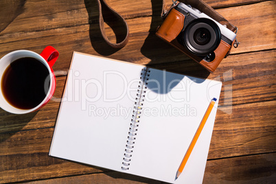 A pen on notepad next to the cup of coffe and camera