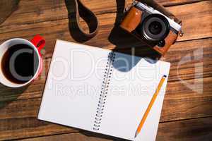 A pen on notepad next to the cup of coffe and camera