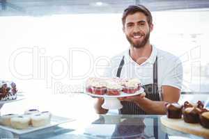 Smiling worker holding cupcakes behind the counter
