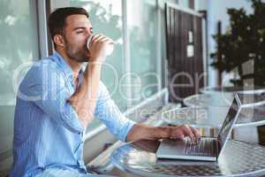 Young businessman drinking coffee beside a laptop