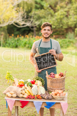 Handsome farmer standing at his stall and holding chalkboard