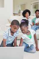 Happy siblings lying on the floor using laptop