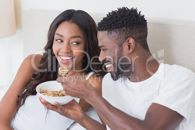 Relaxed couple in bed together eating cereal