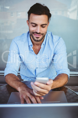 Smiling businessman using phone while working on laptop