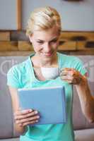 Pretty blonde holding cup of coffee and using tablet computer