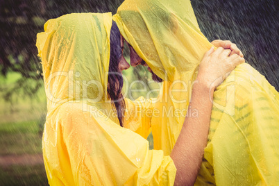 Cute couple wearing protection cape and hugging under the rain