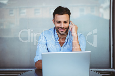 Smiling businessman on the phone working on laptop