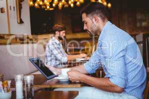 Businessman using tablet while holding cup of coffee