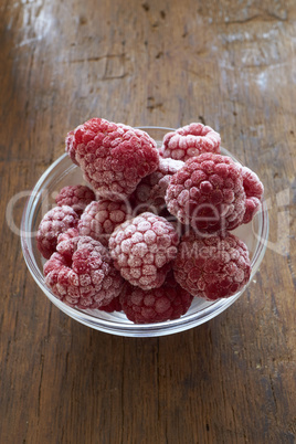 Tiefgefrorene Himbeeren in einer Glasschale auf Holztisch