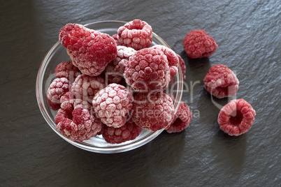 Gefrorene Himbeeren in einer Glasschale auf Schieferplatte