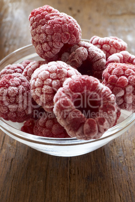 Tiefgefrorene Himbeeren in einer Glasschale auf Holztisch