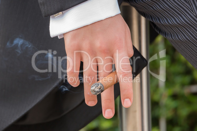 Fingers of man in tails holding cigar