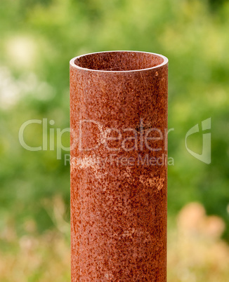 Vertical rusted metal pipe on green