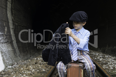 Child in vintage clothes sits on railway road