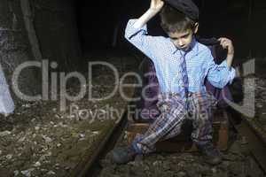 Child in vintage clothes sits on railway road