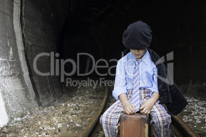 Child in vintage clothes sits on railway road