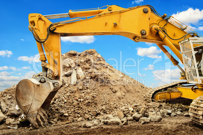 Excavator and heap of dirt in front of blue sky