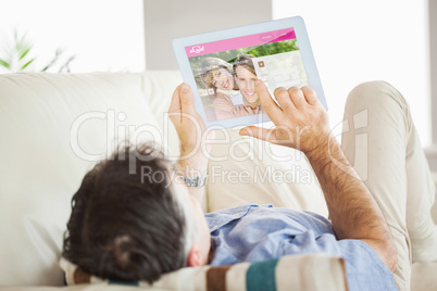 Composite image of man laying on sofa using a tablet pc