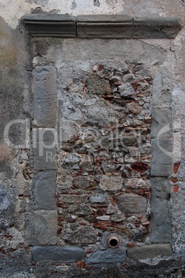 Old window in gray stone wall blocked by bricks and stones