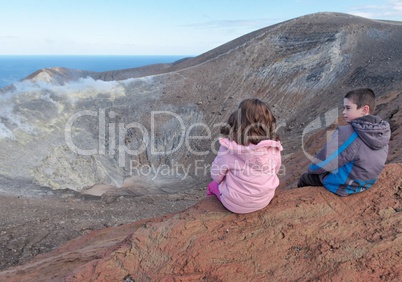 Girl and boy sitting on the rim of volcano crater of Vulcano island near Sicily, Italy