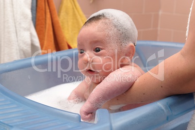 Cute baby in a bathtub with foam cap on his head