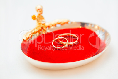 Two wedding rings on a red base with an angel