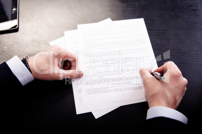 Image of human hand with pen over documents at workplace