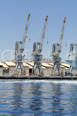 Row of cranes and their reflections in the sea in Eilat harbor, Israel