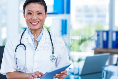 Happy doctor smiling at camera holding tablet