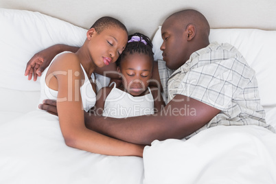 Pretty couple sleeping with their daughter in their bed