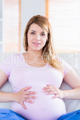 Pregnant woman looking at camera with hands on belly