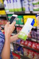 Woman comparing the price of a carton of milk with her phone