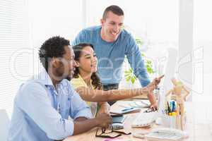 Smiling coworkers using computer together and pointing the scree