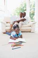 Pretty couple using laptop on couch and their daughter drawing